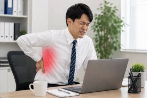 デスクワーク中に背中の痛みを感じている男性