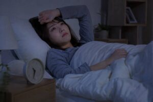 夜中に目が覚めて眠れず時計を確認する女性