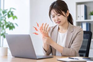 デスクワーク中に手のしびれを感じている女性