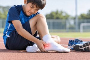 運動後にかかとの痛みを感じて足を押さえる小学生